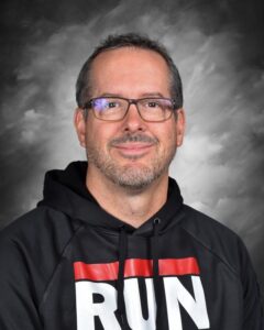 A smiling man with glasses and a beard wears a black hoodie with "RUN" printed on it. The background is gray.