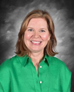 Smiling woman with shoulder-length brown hair wearing a green shirt, against a gray background.