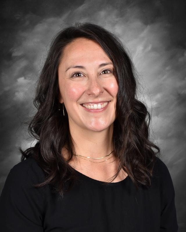 Smiling woman with long dark hair wearing a black shirt against a gray backdrop.
