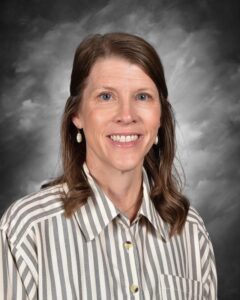 Smiling woman with long hair wearing a striped shirt and earrings, against a gray background.